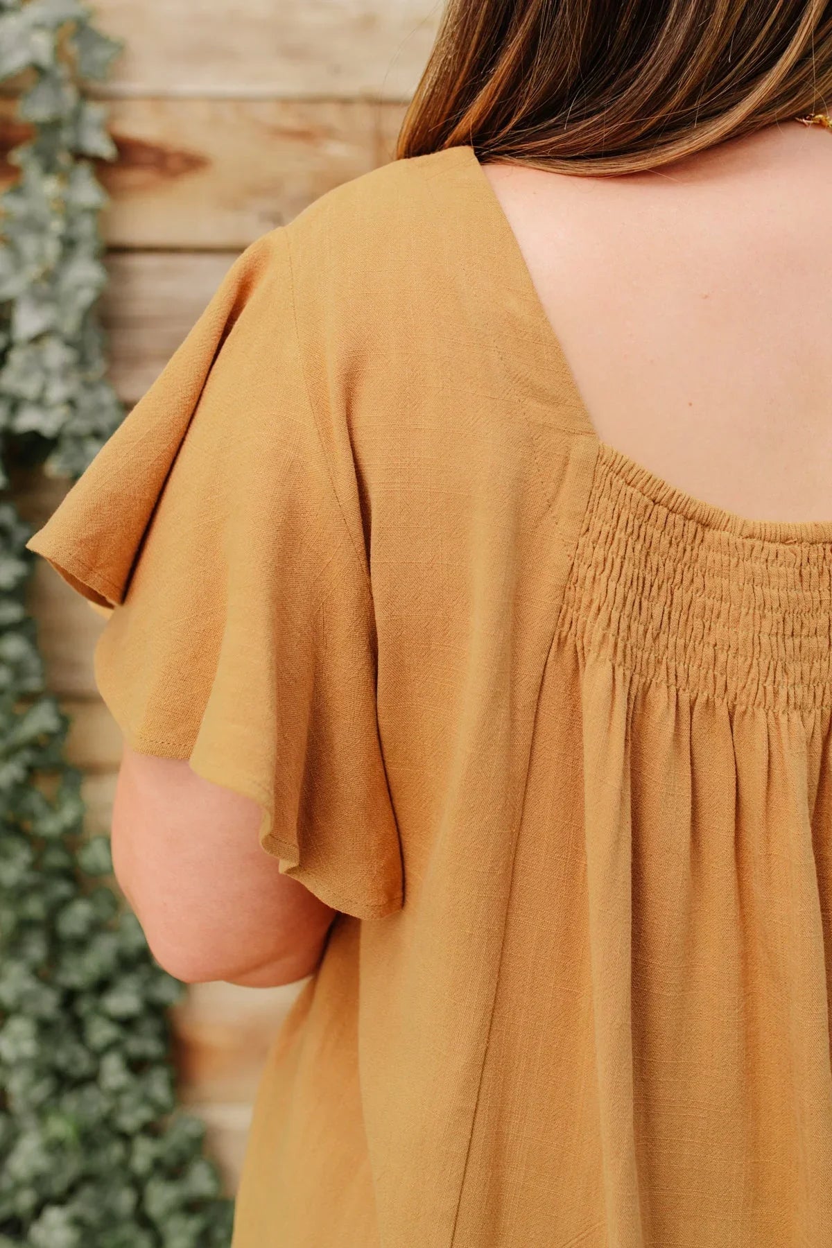 Back view of taupe short sleeve blouse with shirred yoke and relaxed fit.