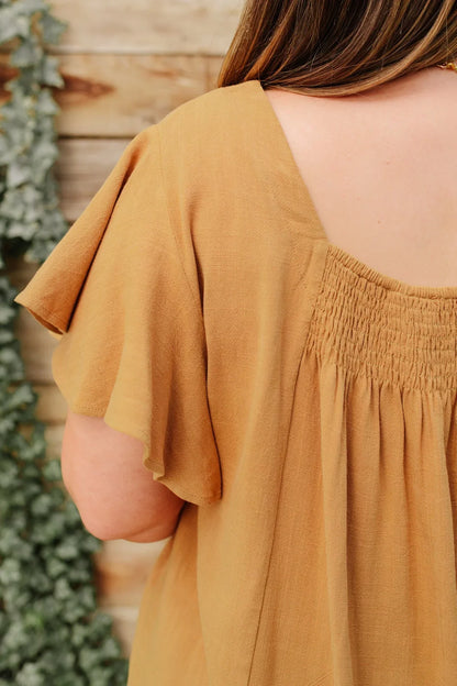 Back view of taupe short sleeve blouse with shirred yoke and relaxed fit.