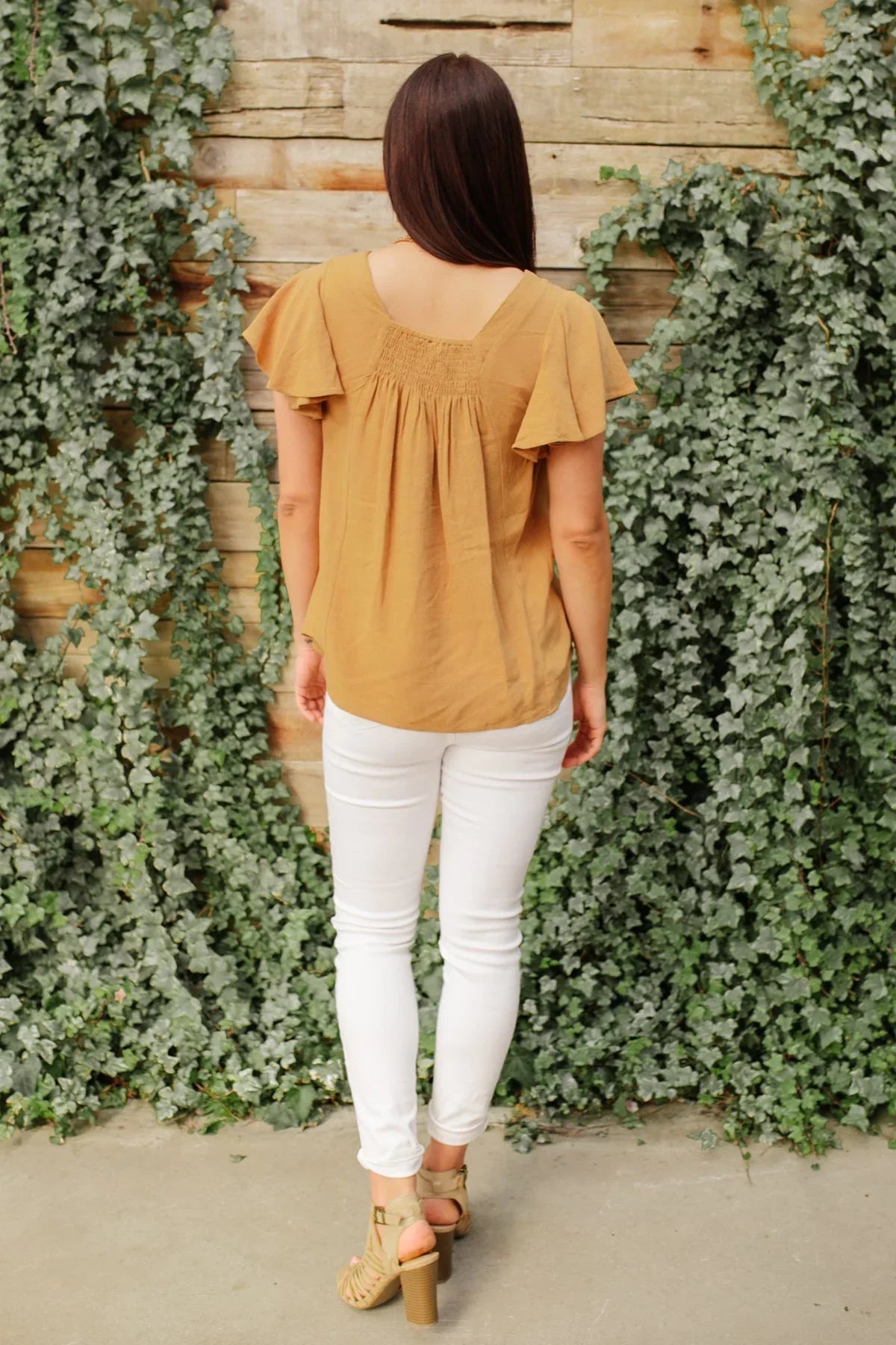 Woman wearing taupe flutter sleeve top and white skinny jeans, standing outdoors