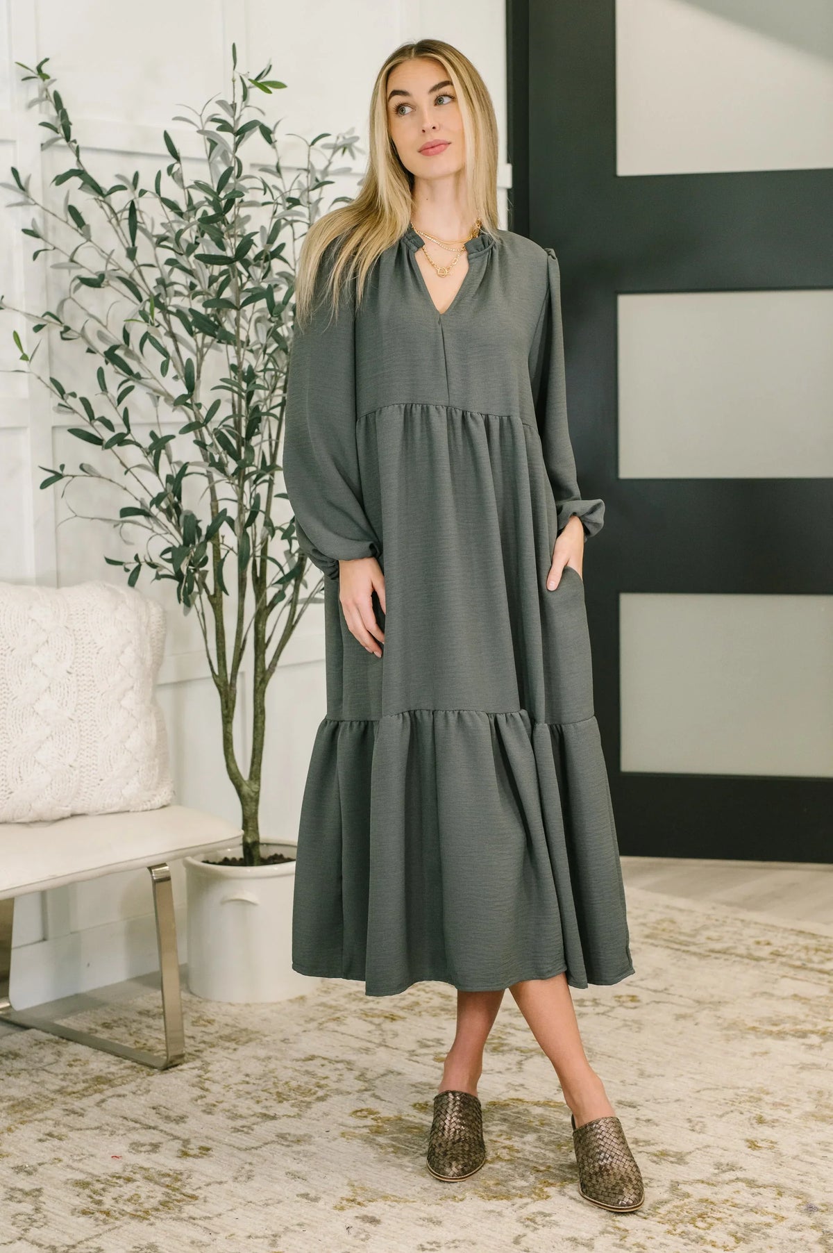 Woman wearing a long-sleeve, dark green tiered V-neck dress in a modern living room