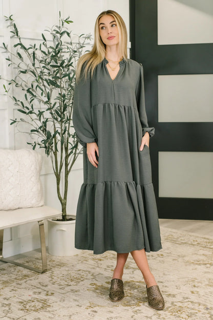 Woman wearing a long-sleeve, dark green tiered V-neck dress in a modern living room