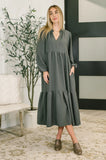 Woman wearing a long-sleeve, dark green tiered V-neck dress in a modern living room