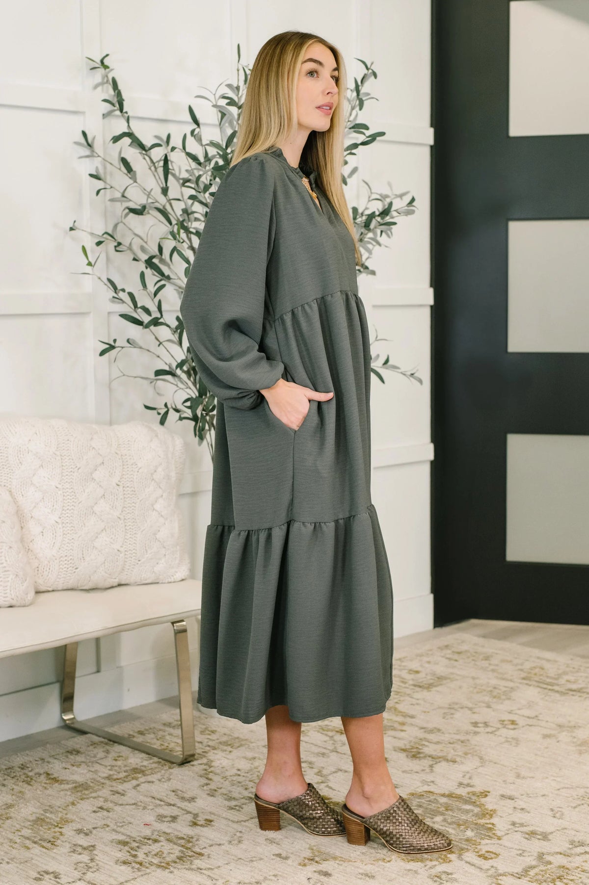 Woman wearing a long-sleeve, tiered V-neck midi dress in dark green, side view indoors