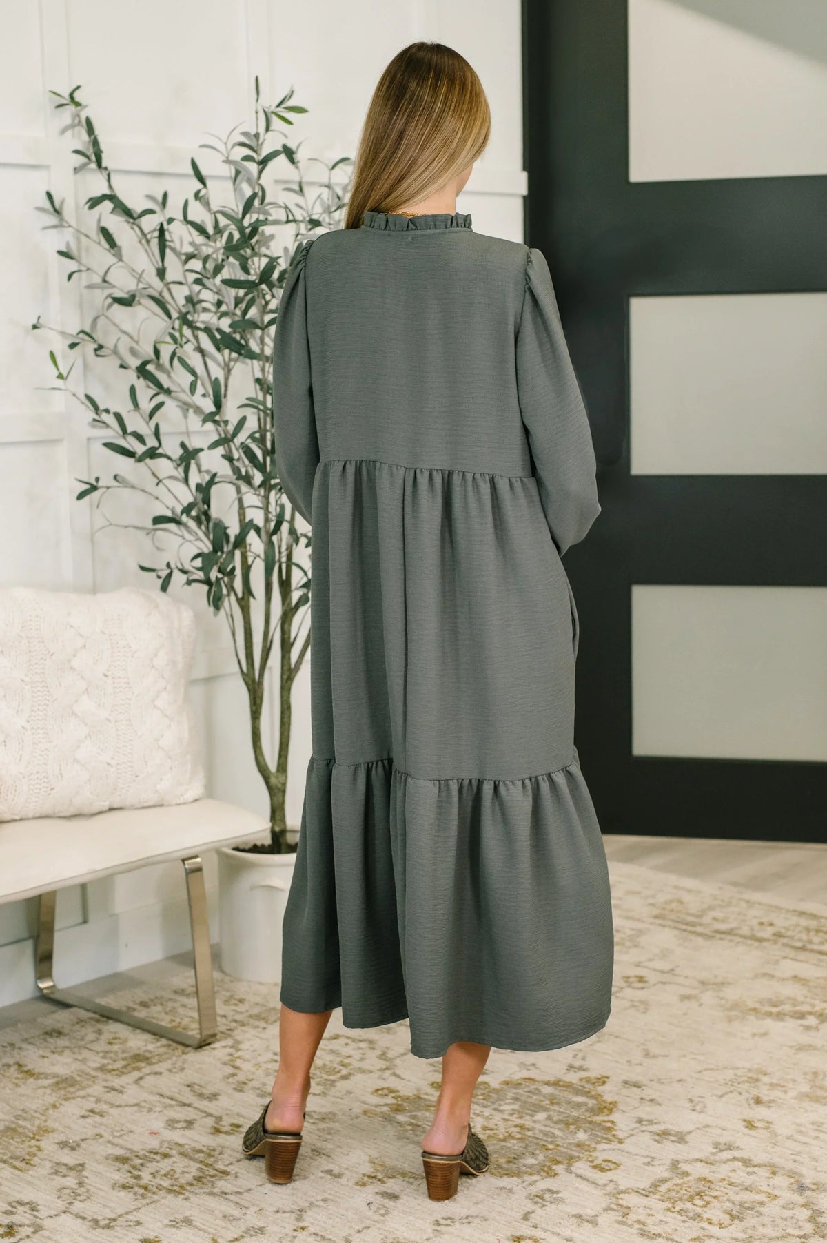 Back view of a woman wearing a long-sleeve, tiered charcoal midi dress indoors