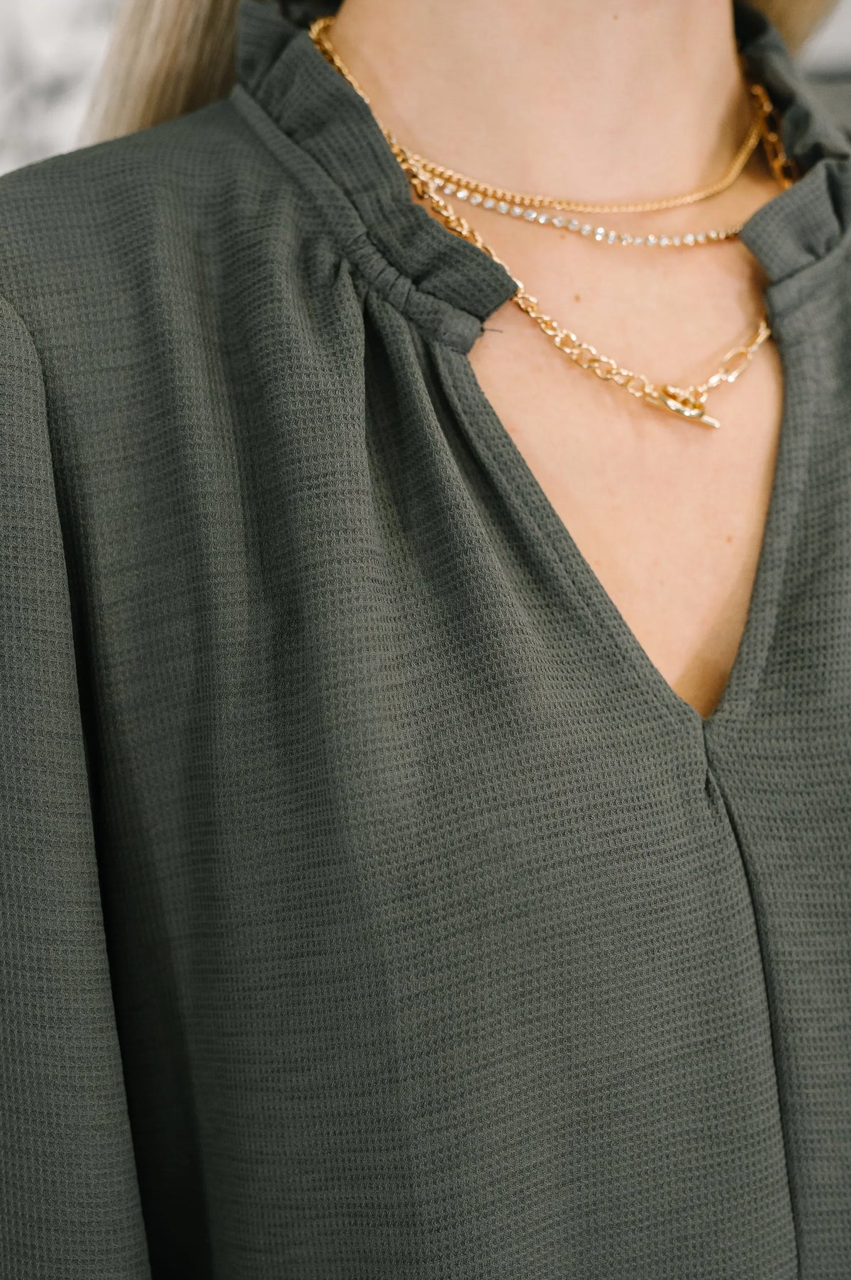 Close-up of textured v-neck tiered dress in dark green with dainty gold layered necklaces.