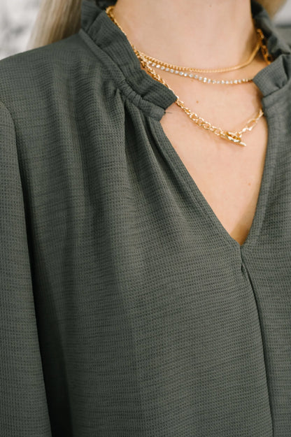 Close-up of textured v-neck tiered dress in dark green with dainty gold layered necklaces.