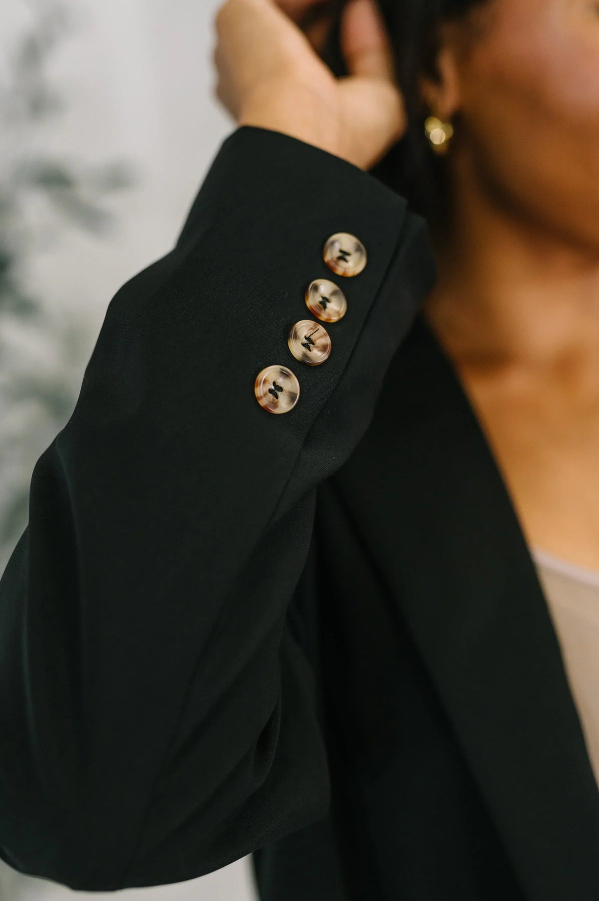 Close-up of black blazer sleeve with four glossy buttons, worn by a woman