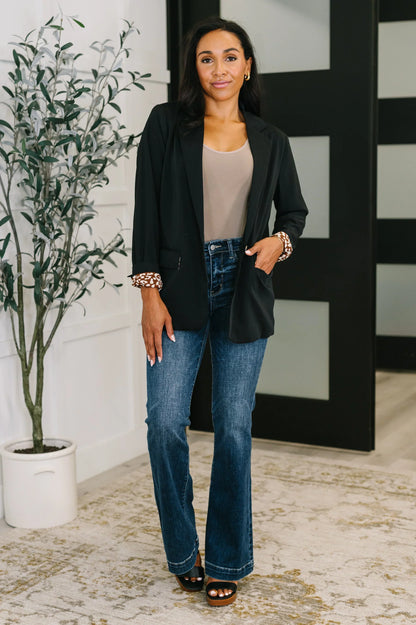 Woman wearing black blazer with patterned cuffs, beige top, and blue jeans in modern room