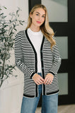 Woman wearing a black and white striped cardigan over a white top and blue jeans indoors.