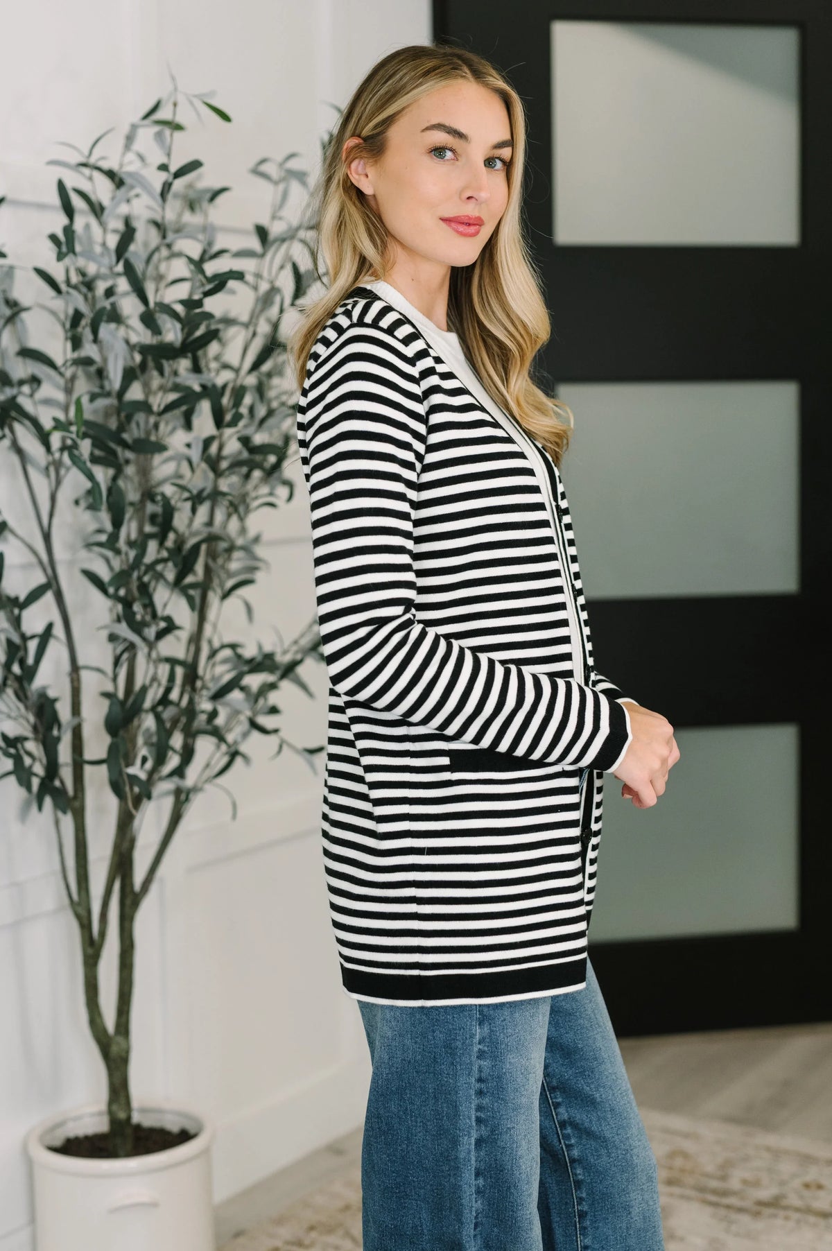 Woman wearing a black and white striped cardigan with blue jeans indoors