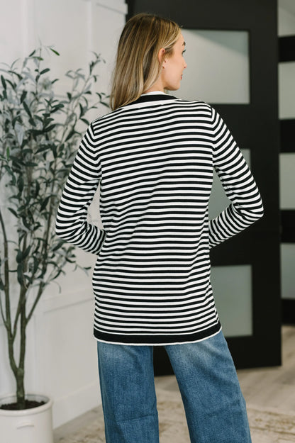Woman wearing black and white striped cardigan with blue jeans indoors