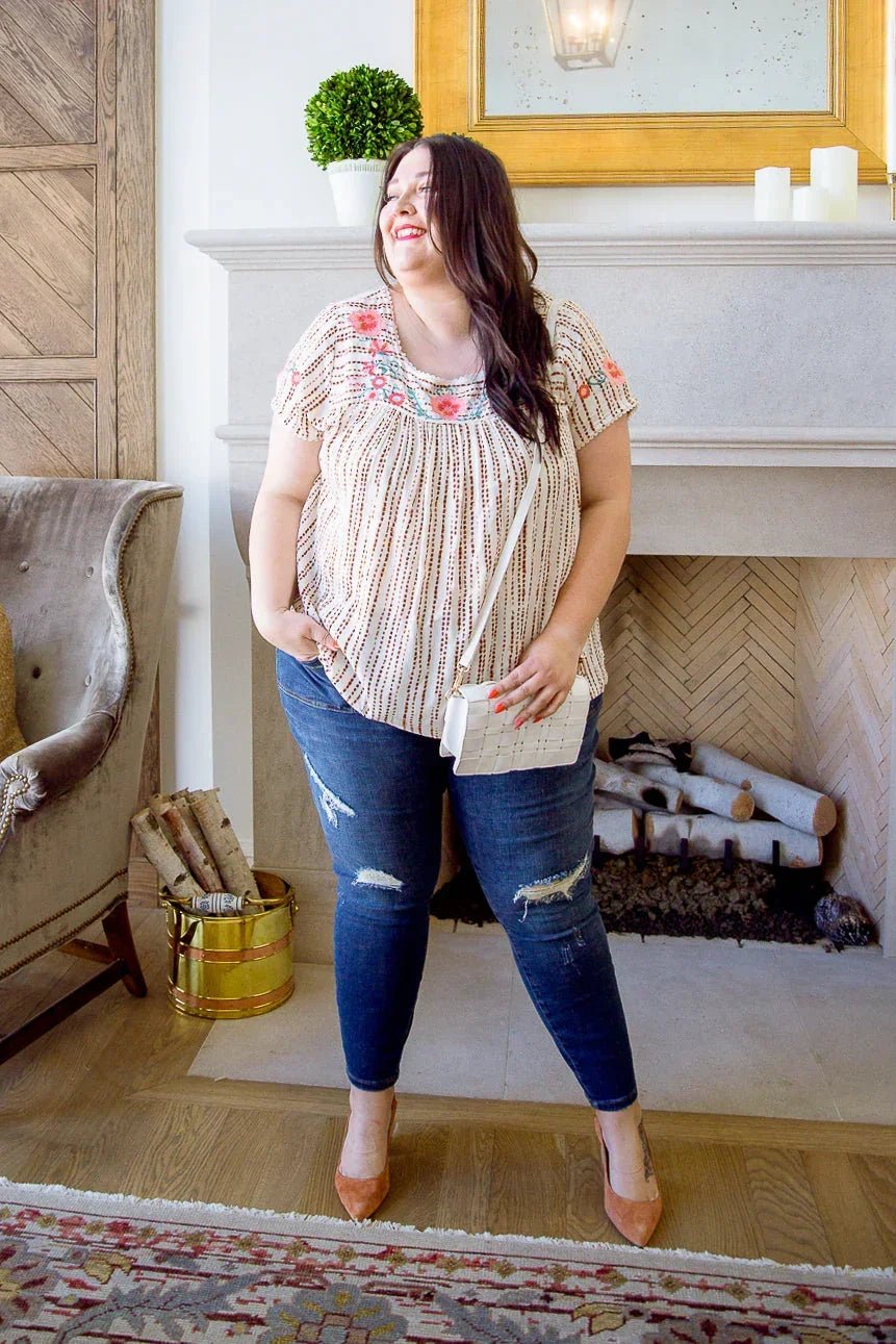 Woman in a floral embroidered blouse and distressed jeans standing in a modern living room