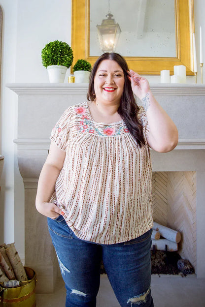 Woman wearing a floral embroidered blouse with relaxed fit and distressed jeans indoors.