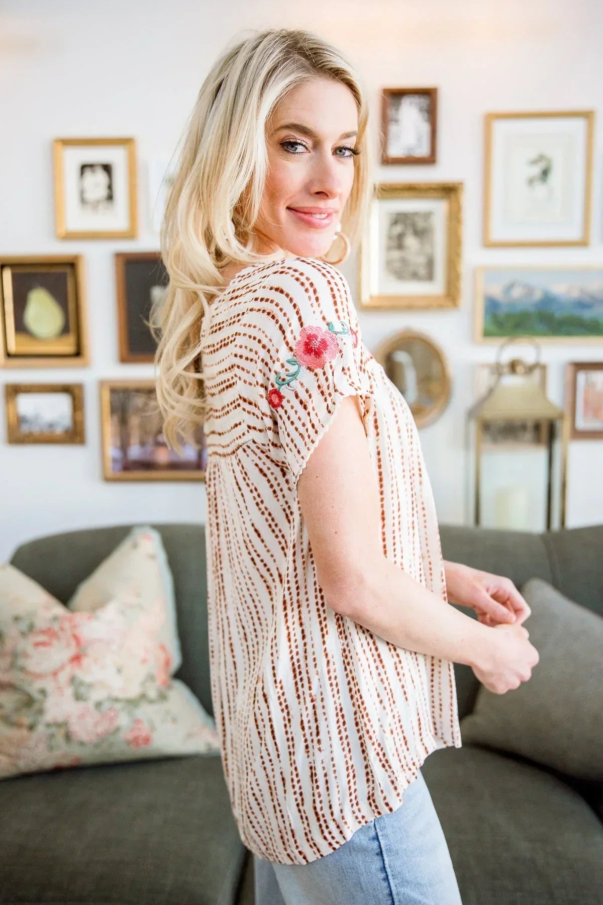 Woman wearing a striped blouse with floral embroidery on the sleeve in a cozy living room setting.