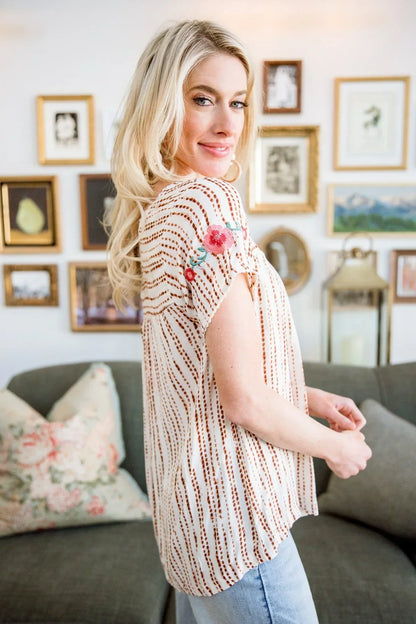 Woman wearing a striped blouse with floral embroidery on the sleeve in a cozy living room setting.