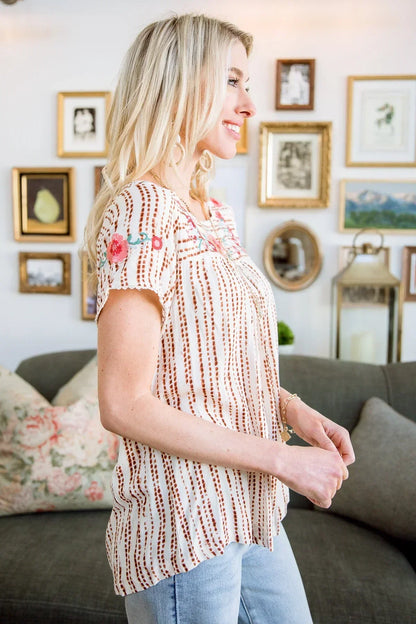 Woman wearing a striped short sleeve blouse with floral embroidery, standing indoors.