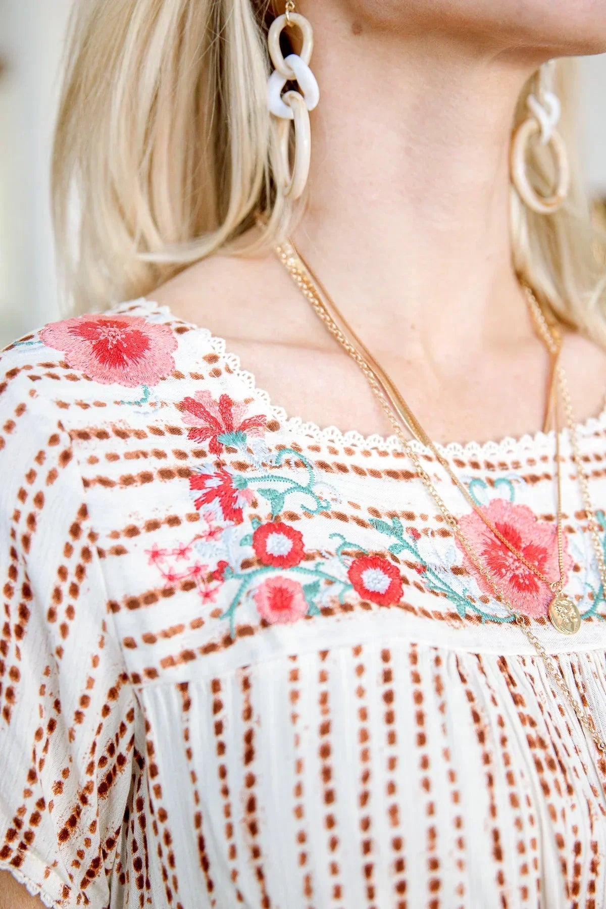 White blouse with brown stripes and floral embroidery, styled with layered necklaces and hoop earrings