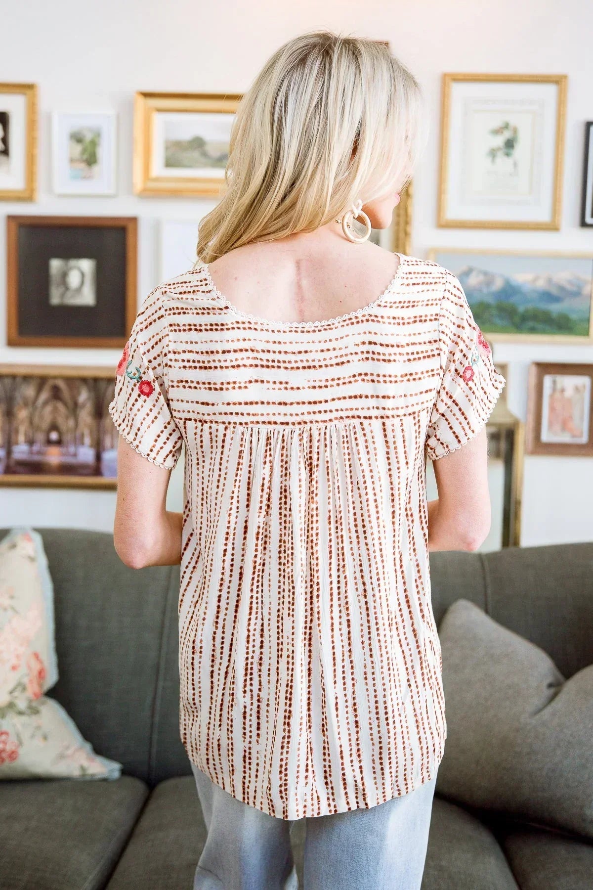 Back view of woman wearing a striped short-sleeve blouse with floral embroidery and relaxed fit.
