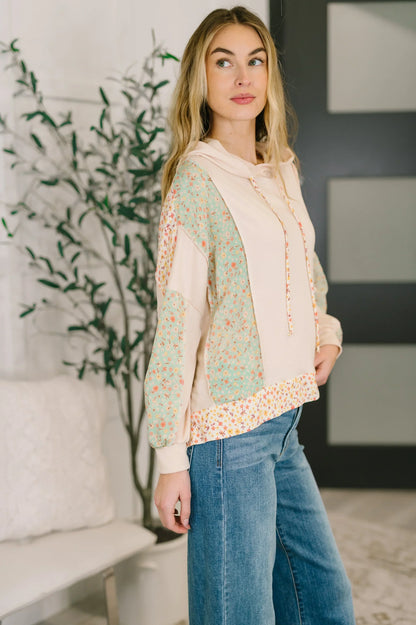 Woman wearing a floral patchwork hooded pullover with relaxed fit and blue jeans indoors