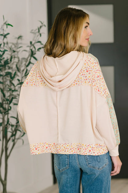 Back view of a woman wearing a floral patchwork hooded pullover with relaxed fit and blue jeans