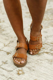 Cognac platform sandals with double buckle straps on a textured neutral rug