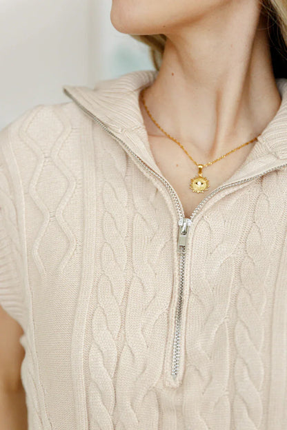Beige cable knit zip sweater with gold pendant necklace, close-up view.