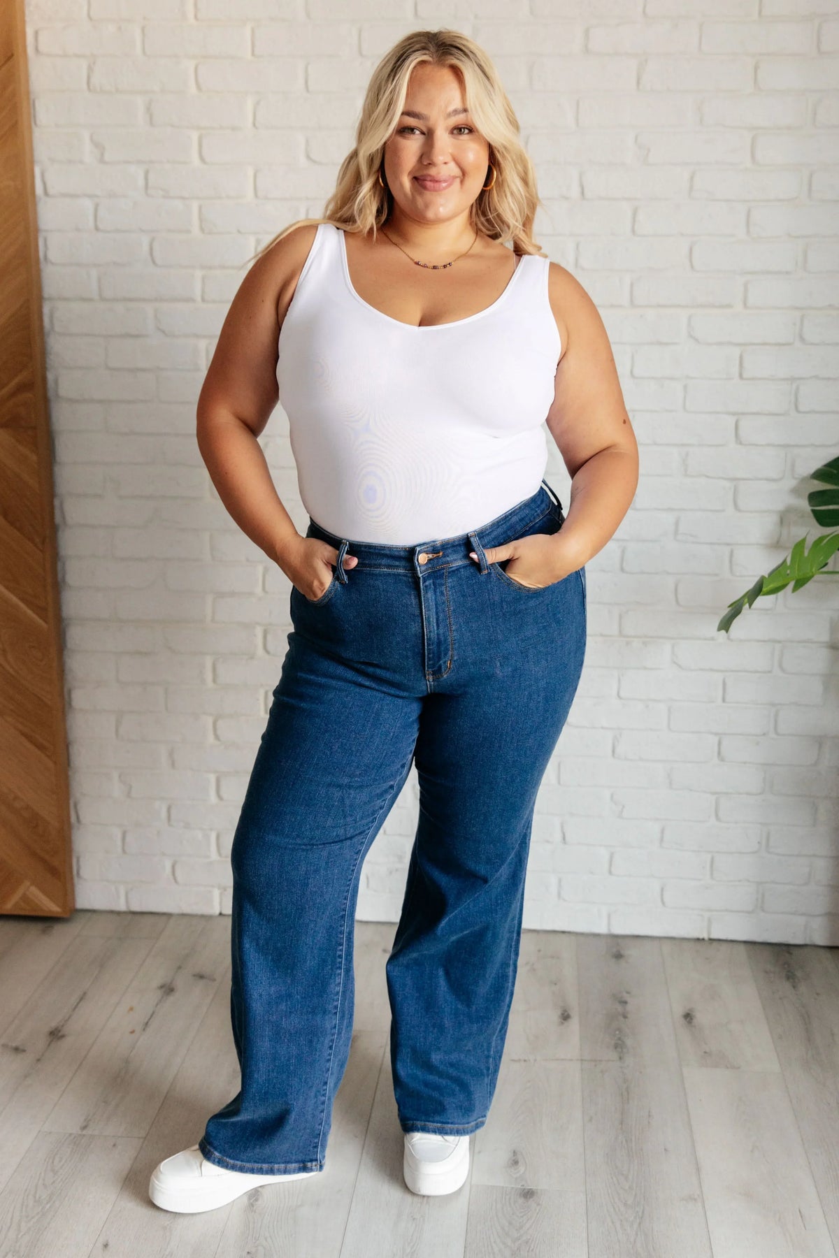 Woman wearing high rise vintage wide leg jeans and white tank top in a modern room