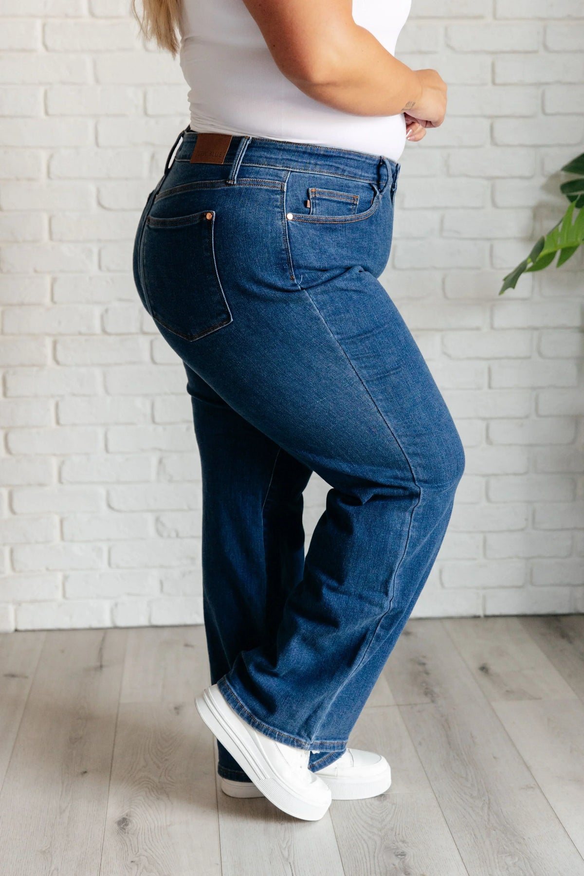 Side view of a woman wearing high-rise vintage wide leg jeans and white sneakers indoors.