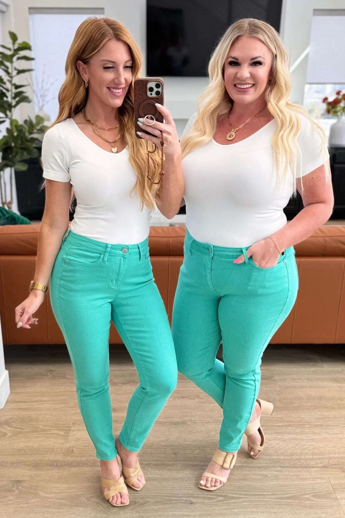 Two women wearing white short sleeve tops and aqua skinny jeans in a modern living room.