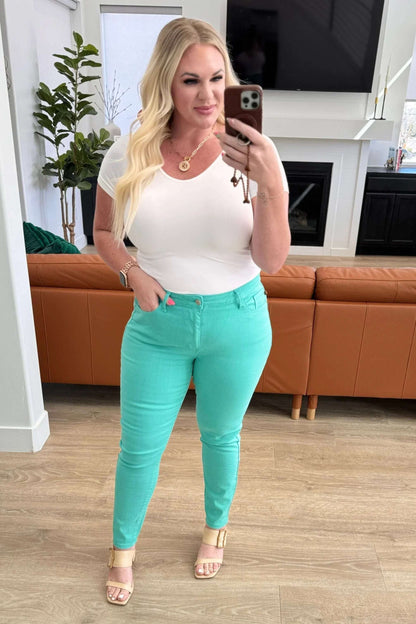 Woman in a white fitted top and mint green skinny pants posing indoors