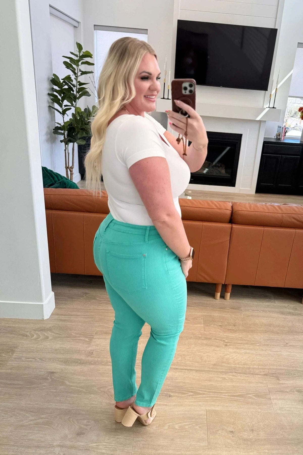 Woman in white top and aqua skinny jeans taking a mirror selfie in a modern living room