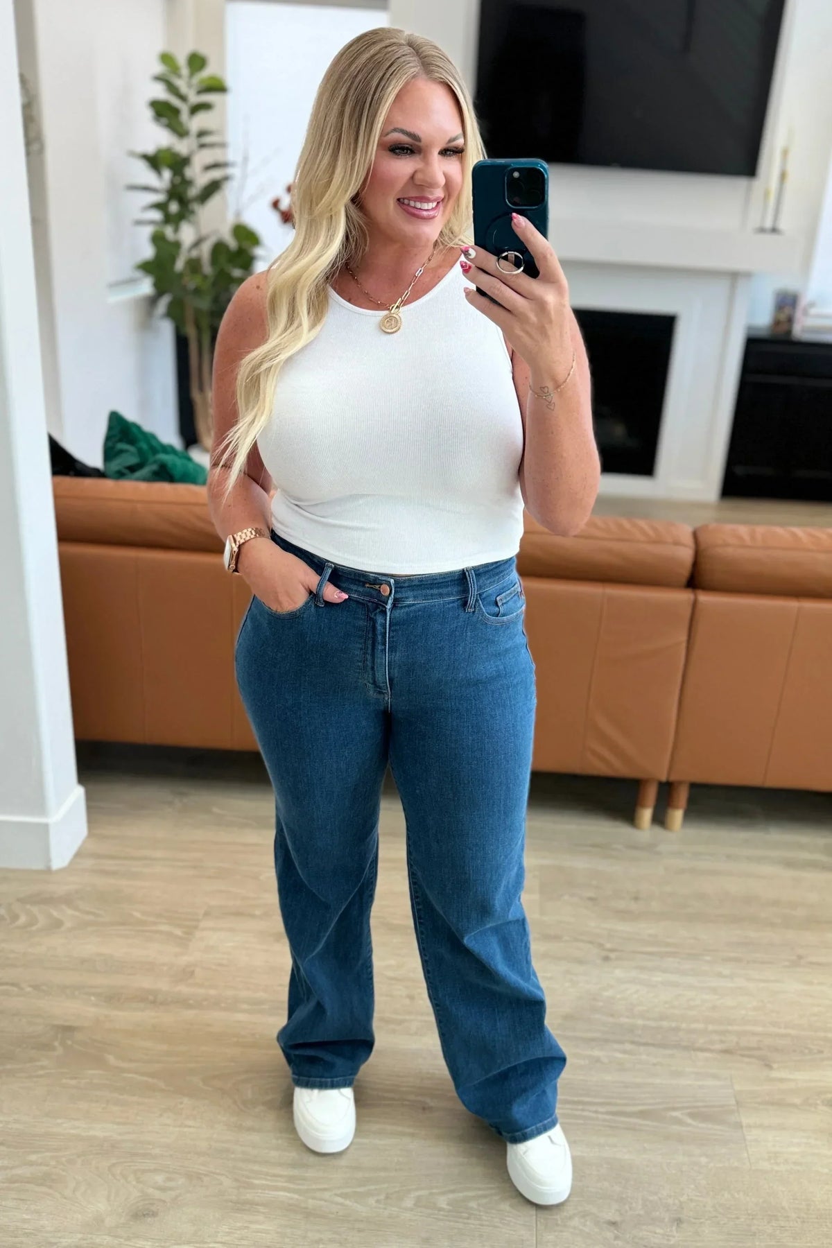 Woman in white sleeveless top and blue high-waisted jeans taking a selfie in a modern living room
