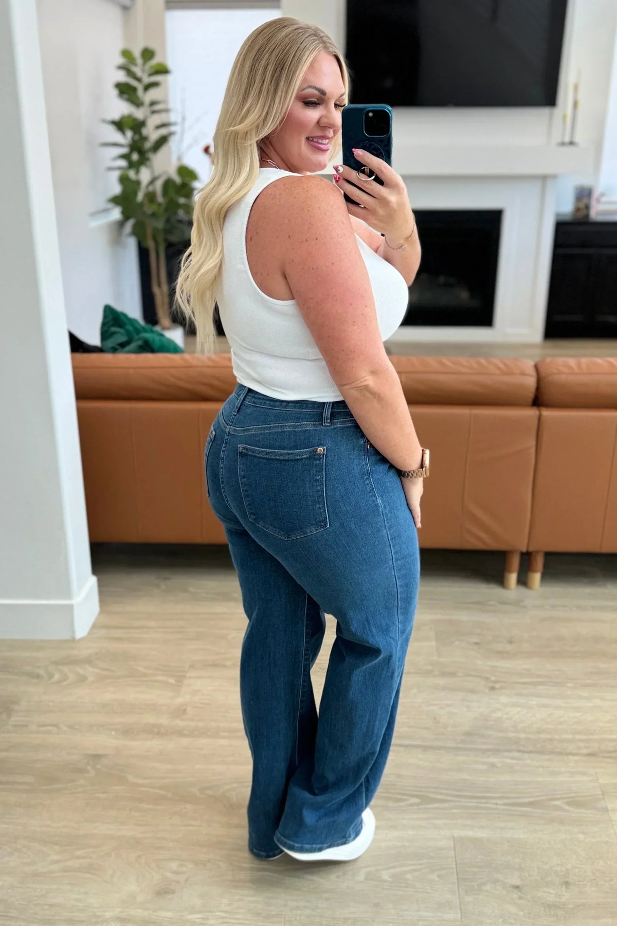 Woman in a white sleeveless top and blue high-waisted jeans standing in a modern living room