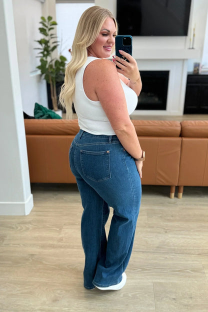 Woman in a white sleeveless top and blue high-waisted jeans standing in a modern living room