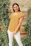 Woman wearing a mustard short-sleeve button front blouse and white pants outdoors