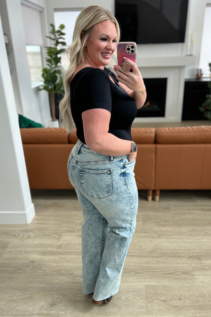 Woman taking a selfie in a living room wearing a black top and light blue jeans.