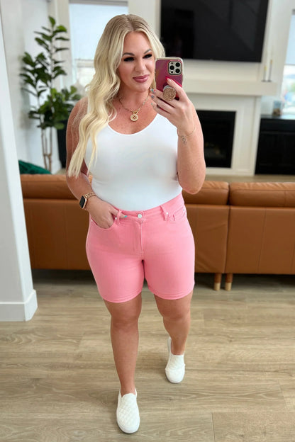 Woman wearing a white tank top and pink denim shorts taking a mirror selfie in a modern living room