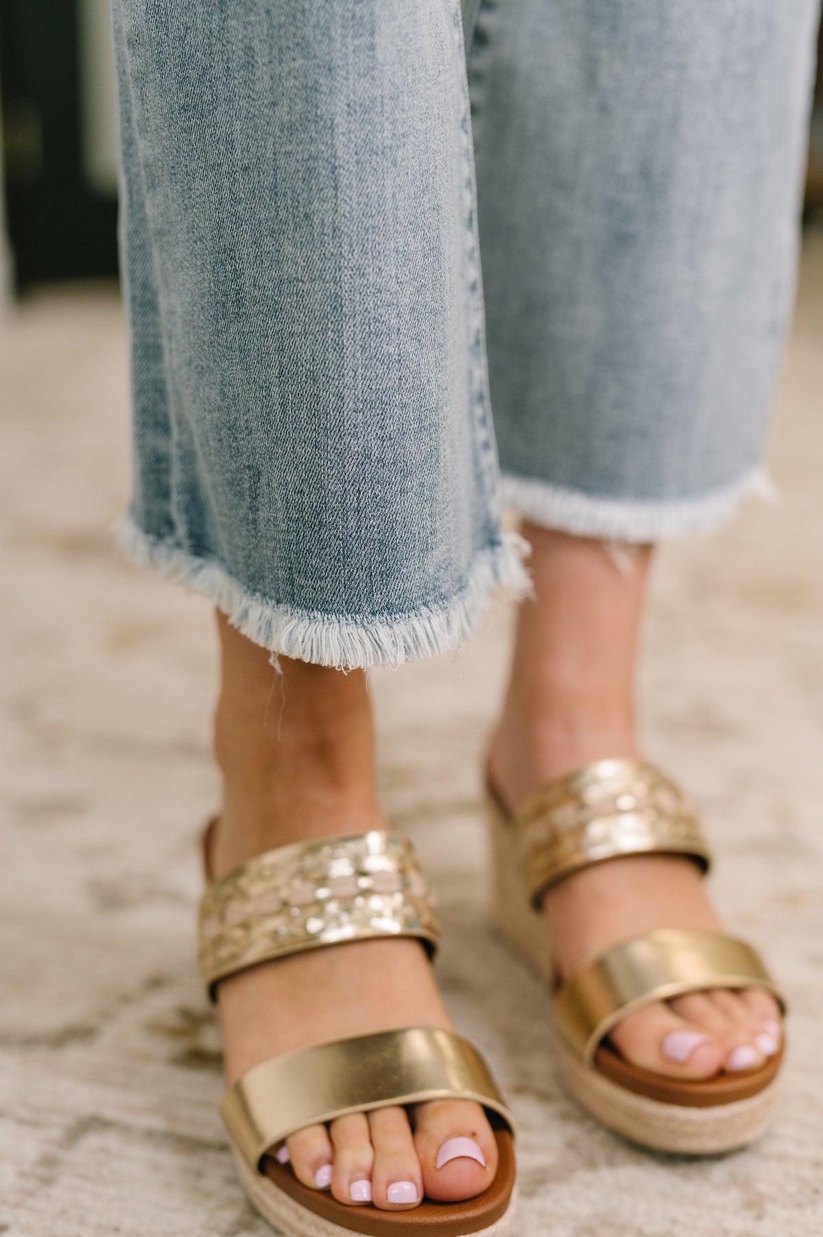 Gold sandals worn with light blue jeans on a neutral background