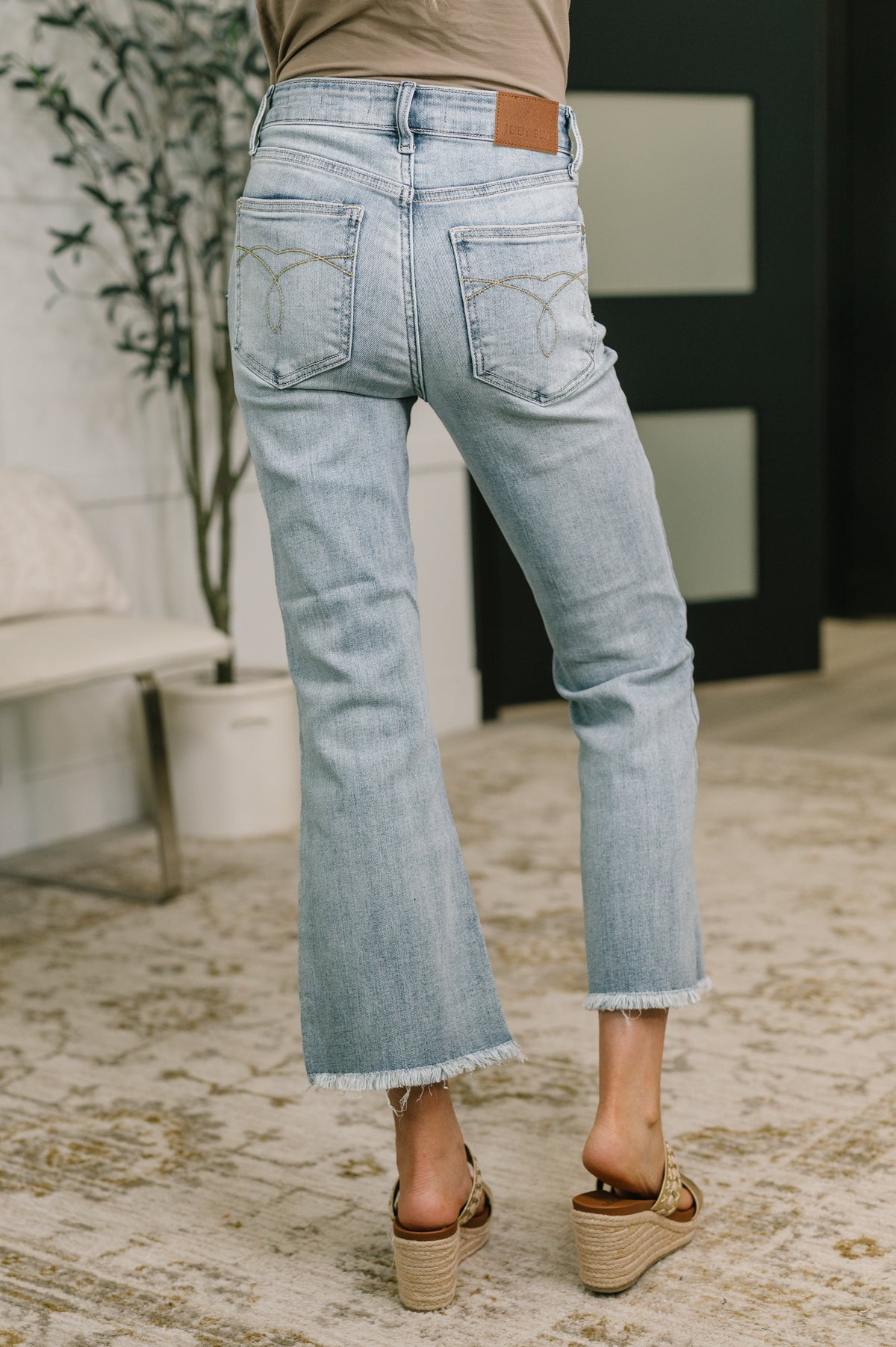 Light blue jeans worn by a person in an indoor setting with a plant and furniture.