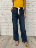 Person wearing blue jeans and a yellow top against a white brick wall.