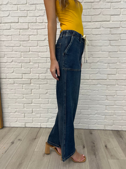Person wearing blue jeans and a yellow top against a white brick wall.