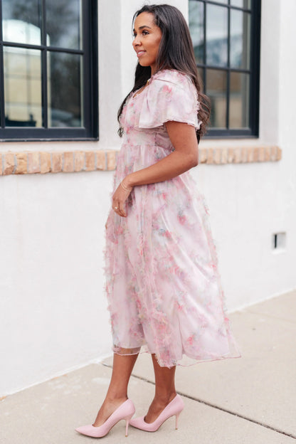 Woman wearing a chiffon floral fluttersleeve dress standing against a white wall.