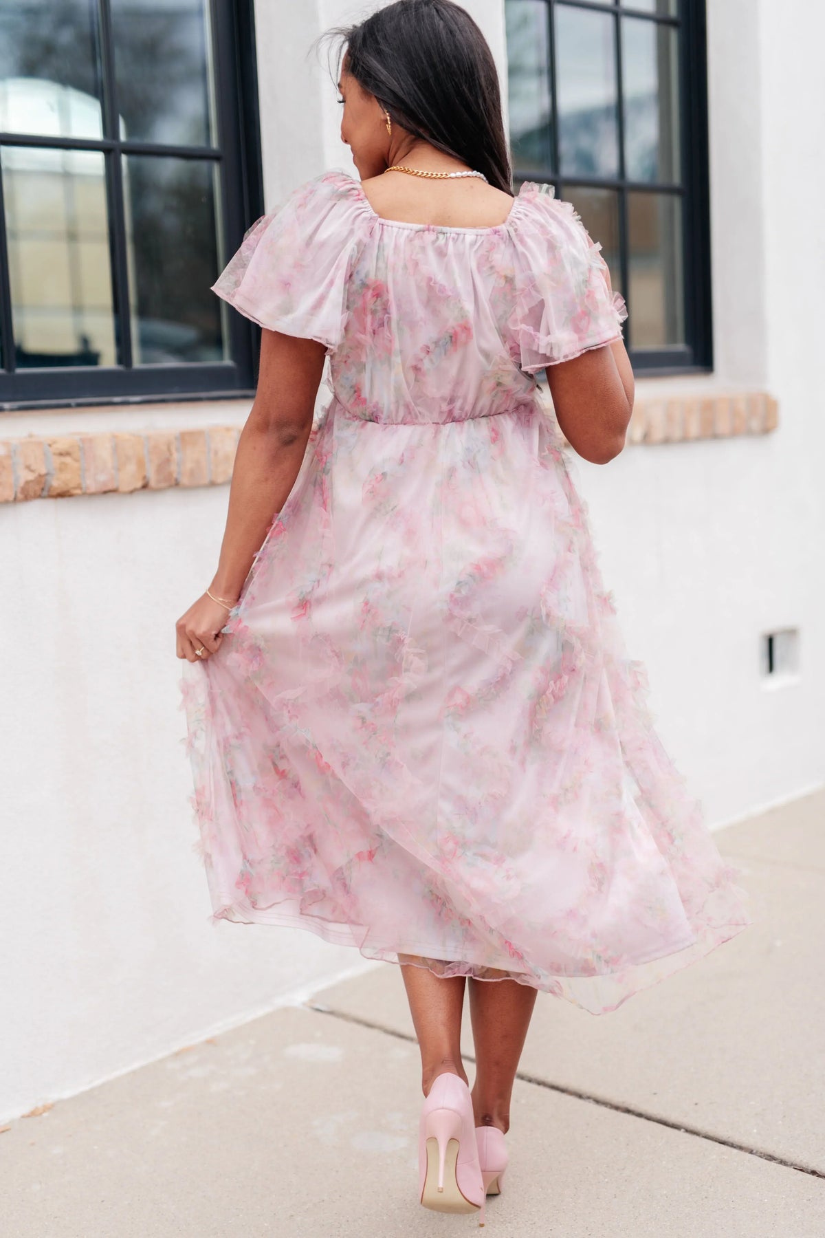 Woman wearing a chiffon floral fluttersleeve dress standing against a white wall.