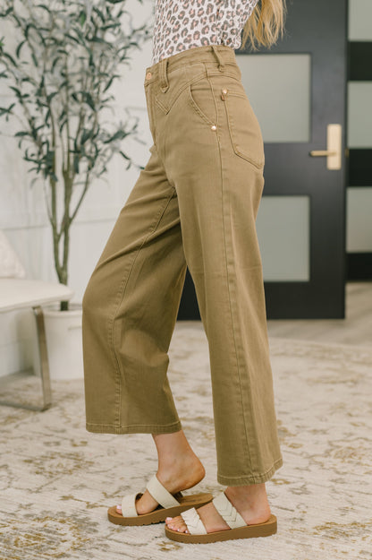 Person wearing beige pants and sandals indoors with a plant and door in the background