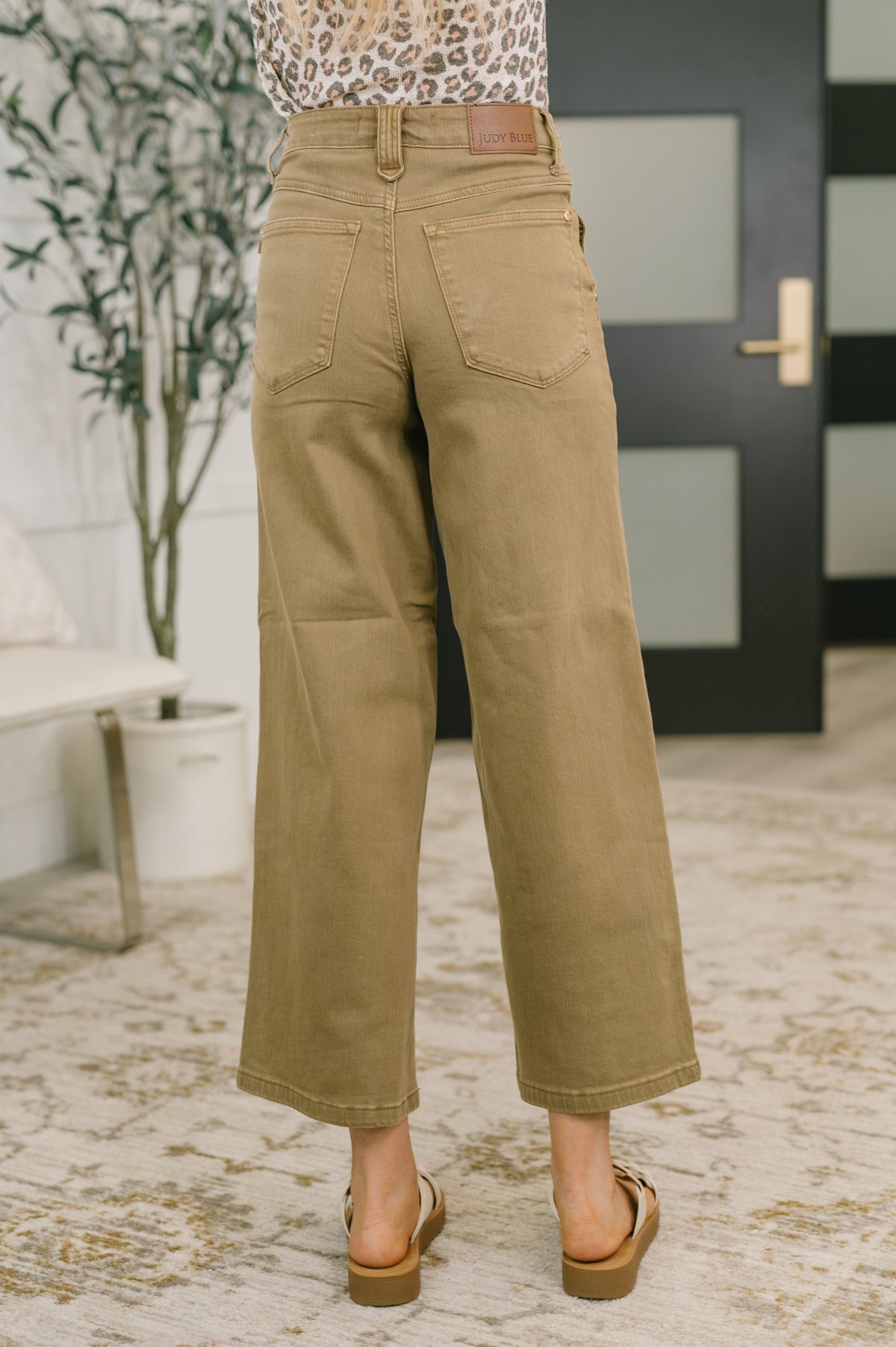 Person wearing tan pants in an indoor setting with a plant and door in the background