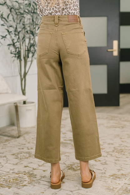 Person wearing tan pants in an indoor setting with a plant and door in the background