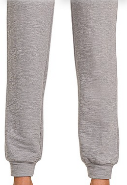 Close-up of a person's legs wearing heather Grey Zenana Cotton Slub Jogger Pants against a plain white background.
