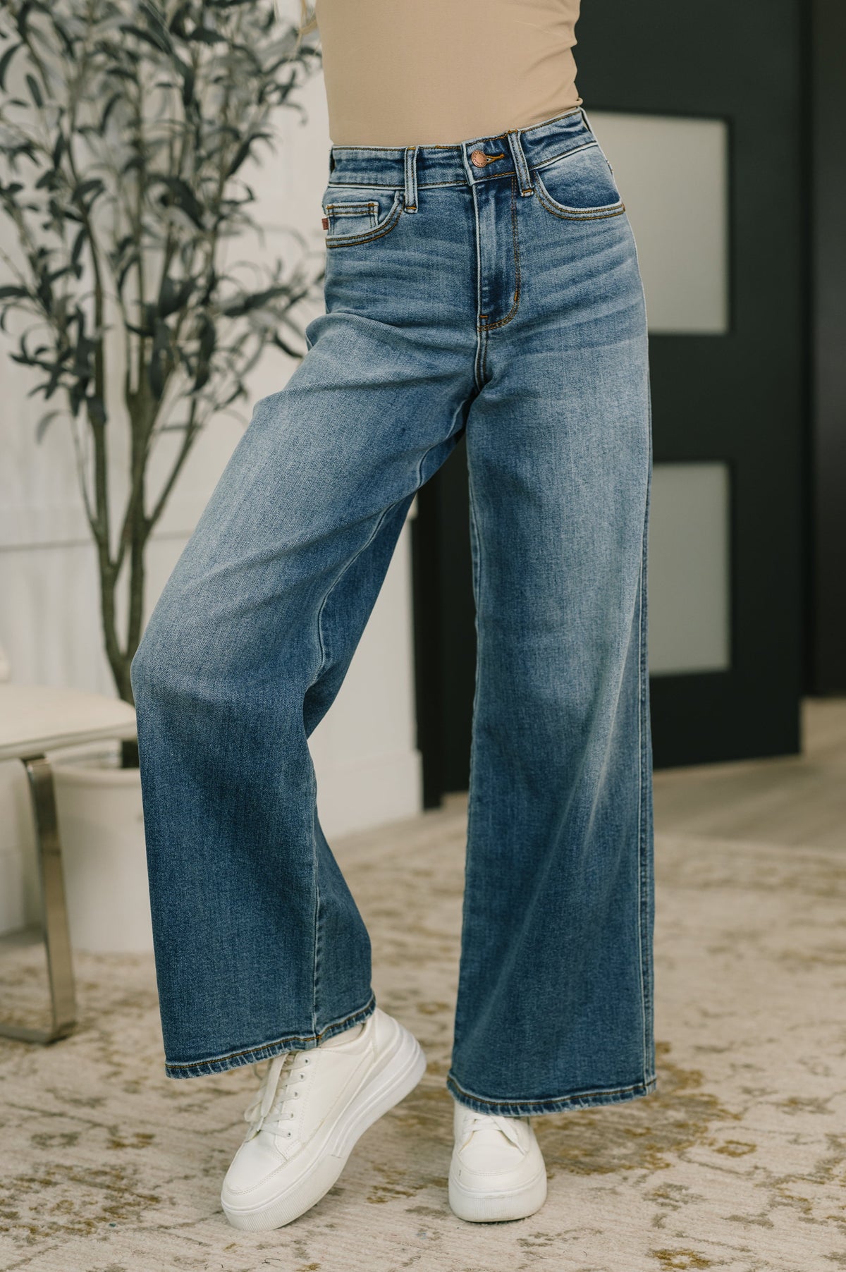 Person wearing blue jeans and white sneakers in an indoor setting