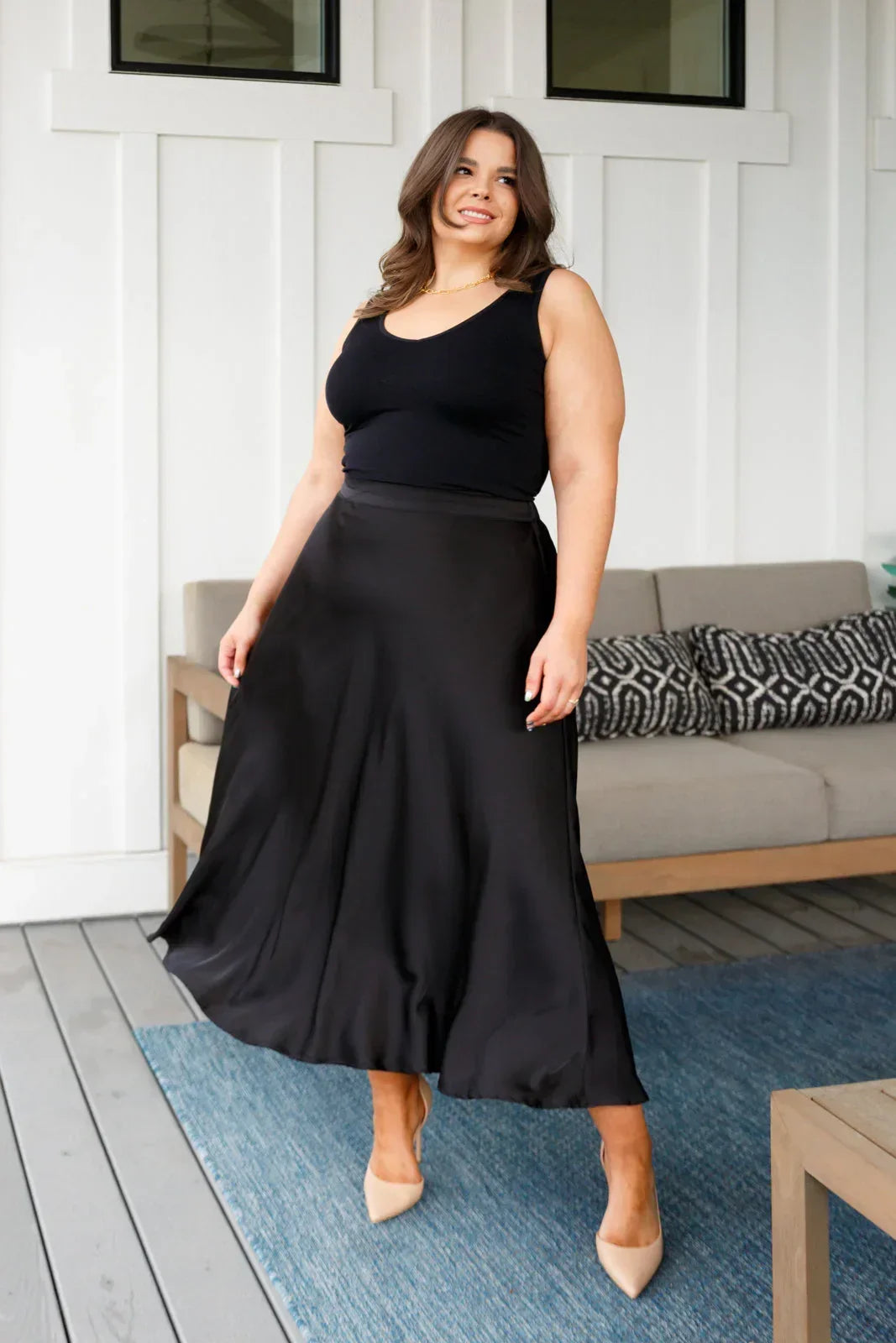 Woman wearing a black sleeveless top and black skirt on a wooden deck.