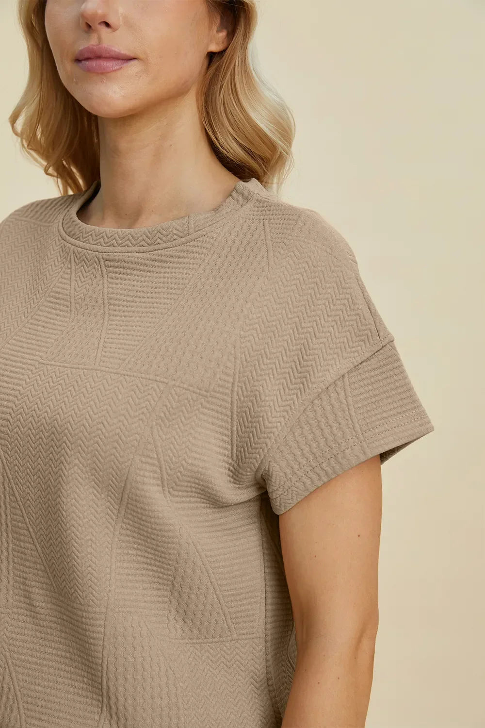 Woman wearing a textured beige short sleeve knit top with crew neckline